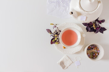 Obraz na płótnie Canvas Cup of ginger tea composition with teapot, tea bag and purple leafs on white background. Flat lay, top view. 