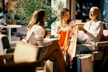 Three shopaholics are sitting at a coffee shop and showing each other clothing they bought for a special occasion.