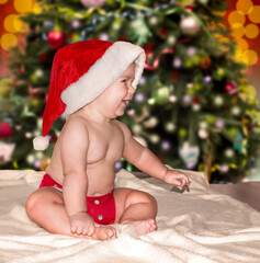 Obraz na płótnie Canvas Beautiful child in red santa hat sits near the christmas tree