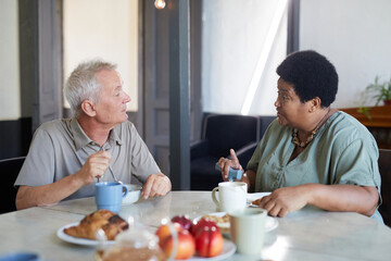 Fototapeta na wymiar Side view portrait of two senior people enjoying breakfast at table in modern nursing home