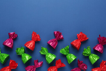 Many candies in colorful wrappers on blue background, flat lay. Space for text