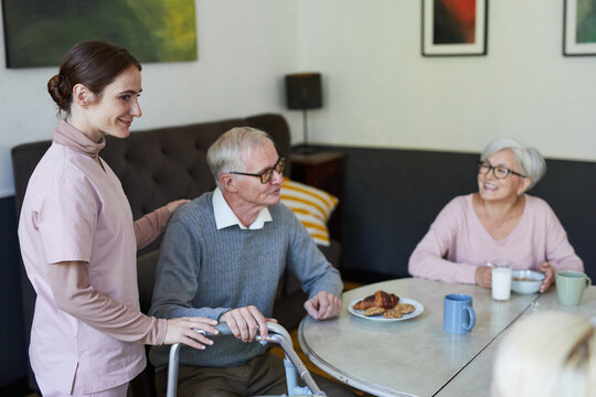 Side view portrait of smiling young woman assisting senior people in nursing home during dinner, copy space