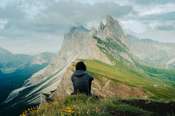 Fototapeta premium Man from behind sitting on the cliff of Seceda mountains.