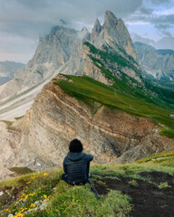 Man from behind sitting on the cliff of Seceda mountains.