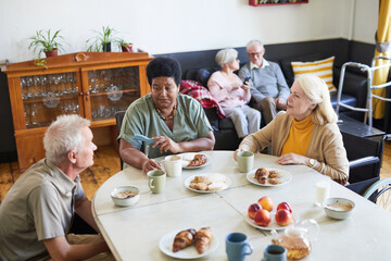High angle view of diverse group of senior people enjoying breakfast in cozy nursing home, copy space - obrazy, fototapety, plakaty