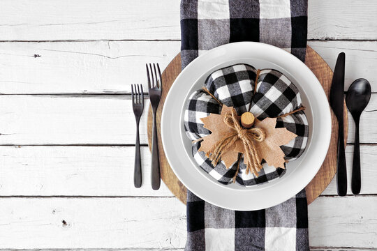 Autumn harvest or thanksgiving dinner table setting with buffalo plaid pumpkin and napkin, plates and flatware. Overhead view on a white wood background. - Powered by Adobe