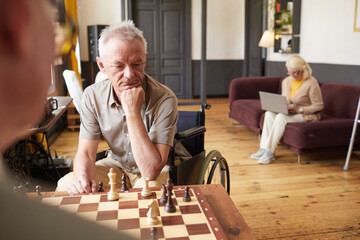 Portrait of two senior men playing chess and enjoying activities in cozy nursing home, copy space