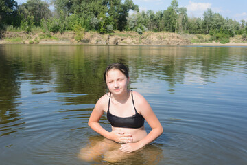 Girl teenager sits in water of the river summer beach. Abdominal pain from bathing in dirty water