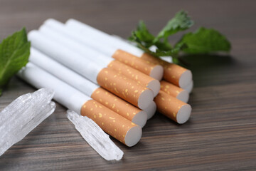 Cigarettes, menthol crystals and mint on wooden table, closeup