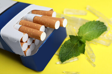 Pack of cigarettes, menthol crystals and mint on yellow background, closeup