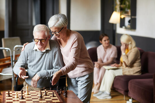 Portrait Of Two Senior People Playing Chess And Enjoying Activities In Retirement Home, Copy Space