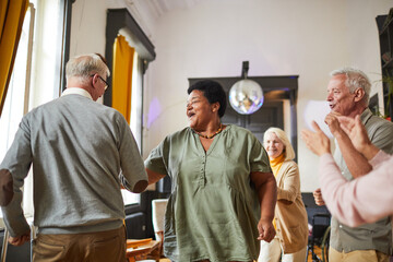 Diverse group of smiling senior people dancing while enjoying activities in retirement home, copy space - Powered by Adobe