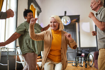 Portrait of smiling senior woman dancing and looking at camera while enjoying activities in retirement home, copy space