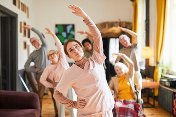 Waist up portrait young woman coordinating group of senior people enjoying morning exercises in...