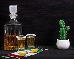 shots of tequila with bottle on wooden table on a flag of viva mexico and salt and lemon slices