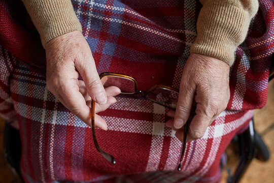 Top view close up of senior woman holding eyeglasses while sitting in whellchair covered by blanket