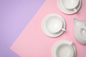Cups with saucers and teapot on color background, flat lay. Space for text