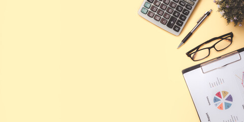 Office desk with analysis chart or graph, pen, eyeglass and calculator on yellow background. Top...