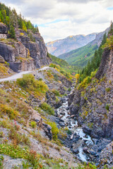 Dirt road in the mountains dangerously close to edge of canyon with river at bottom