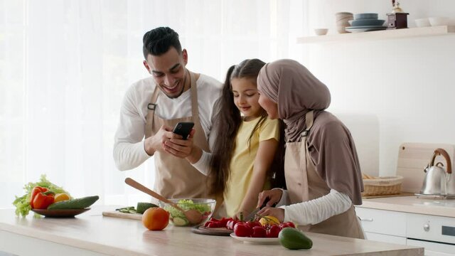 Middle-Eastern Husband Taking Photos Cooking With Wife And Daughter Indoor