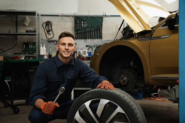 Fototapeta na wymiar Portrait of professional mechanic with car wheel at automobile repair shop