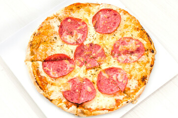 Tasty salami pizza with tomato sauce, cheese and fresh basil, on a white plate