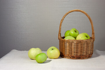 Food, fruits. Wicker basket with green apples on a light gray background. Rustic background. Selective focus