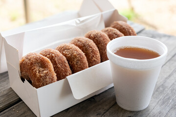 Cup of apple cider and half dozen of cinnamon donuts on wooden table