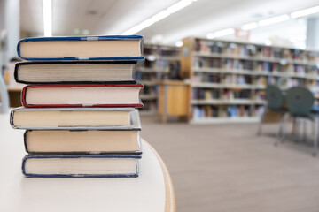 Stack of books on table against bookshelf at library for education, literature or wisdom concept