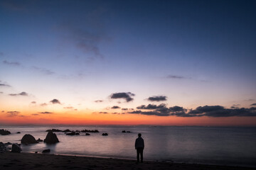 A man stands before the Kunisaki coast line in early morning. Sunrise sky over a rocky beach in early morning near Oita city, Japan. A seascape photo in Kunisaki japan 