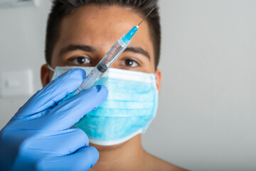 young latin male with surgical mask, shirtless, with syringe in hand prepared for vaccination, Rembrandt lighting (45° light) latex gloves (covid-19, influenza) pandemic and health concept