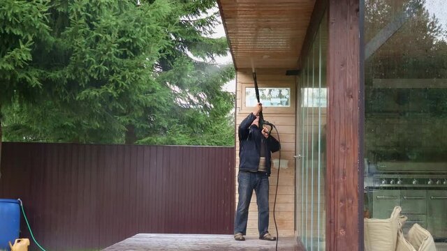 Man cleaning walls and floor with high pressure power washer. Washing terrace wood planks and cladding walls. High quality 4k footage