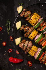Skewers with beef, corn, paprika, zucchini, red onion and thyme on a black plate with dark background