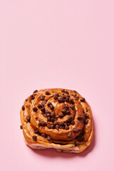 Sweet roll bread with chocolate chips isolated on pink background. Vertical photo. Top view angle. Food and healthy concepts.