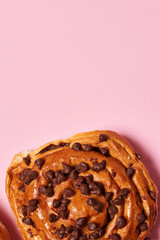 Close up of sweet roll bread with chocolate chips on pink background. Vertical photo. Top view angle. Food and healthy concepts.