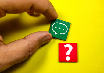Hand holding wooden cubes with the letters Q and A or questions and answers on a yellow background.