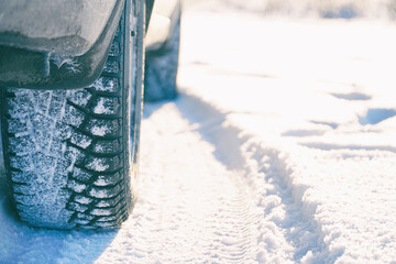 Studded winter car tires on snow-covered road in the sunlight