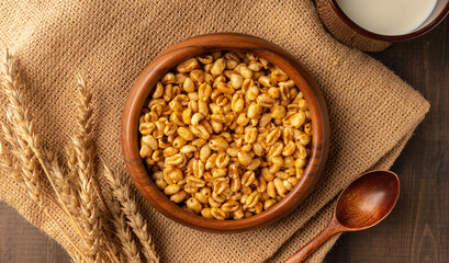 Wheat flakes cereal breakfast in wooden bowl with dry spikelets on the rustic background. Selective focus.