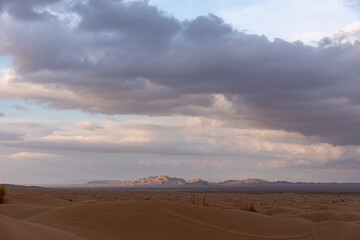 Fototapeta na wymiar Nature and landscapes of dasht e lut or sahara desert with sand dunes in foreground and cloudy evening sky and mountain in background