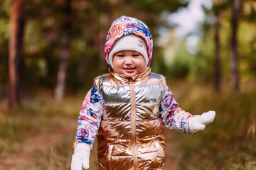 two-year-old girl in golden vest walks in the forest in autumn