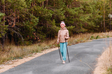elderly sixty-year-old woman in sportswear is engaged in Nordic walking with sticks in the forest in the autumn