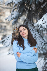 A beautiful girl walks in the winter forest with an owl. Artistic photo session with an owl. Winter forest.