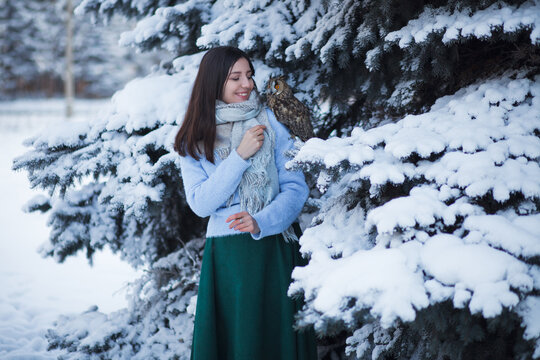 A beautiful girl walks in the winter forest with an owl. Artistic photo session with an owl. Winter forest.