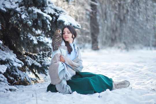 A beautiful girl walks in the winter forest with an owl. Artistic photo session with an owl. Winter forest.