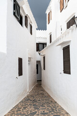 Fototapeta na wymiar Narrow cobble stone street between white solid buildings in Menorca, Spain