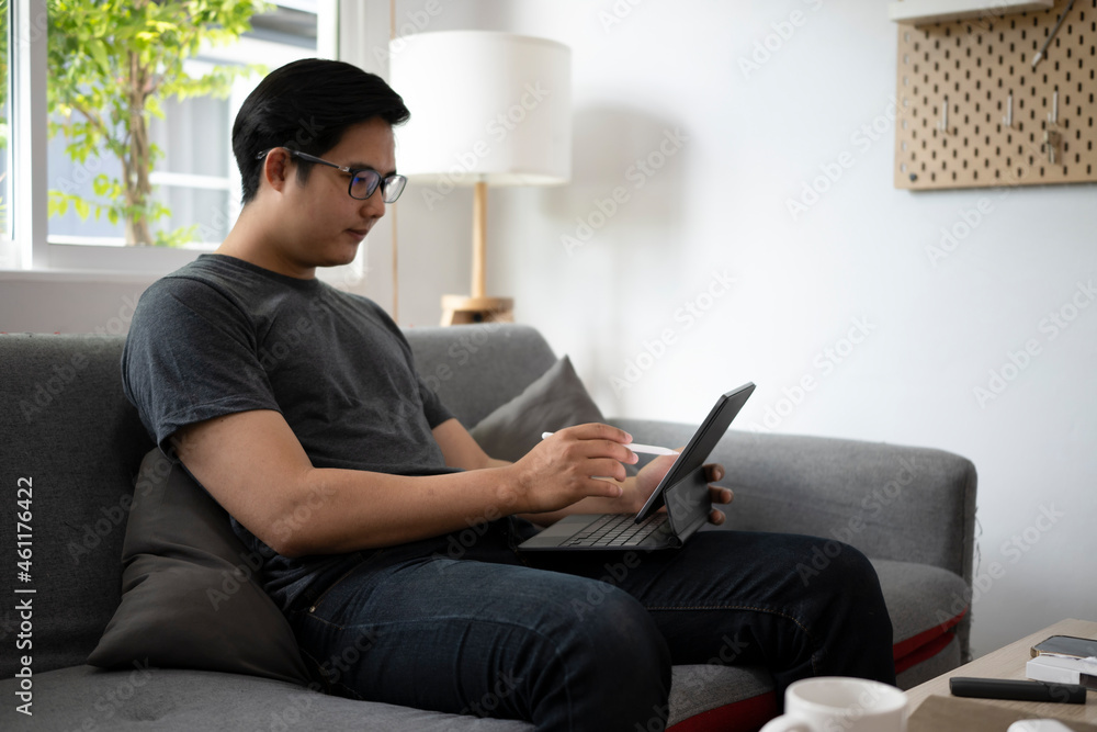 Poster handsome asian man resting on couch and browsing internet with computer tablet.