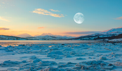 Fototapeta na wymiar Panoramic view at fjord with coast of the Norwegian Sea in the background snowy mountains Arctic Circle at sunset - As a result of melting snow, freezing of the water mixed with the sea - Norway