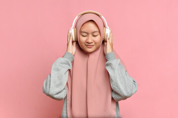 A young muslim girl listens to her favorite music in white headphones, closing her eyes from pleasure, enjoyment, music lover