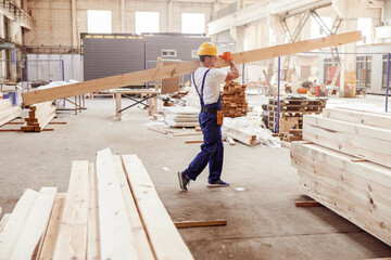 Male builder carrying wooden plank at construction site