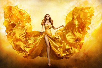 Fashion Woman in Yellow Gown. Fantasy Girl in Golden Dress Flying on Wind like Phoenix Wings in...